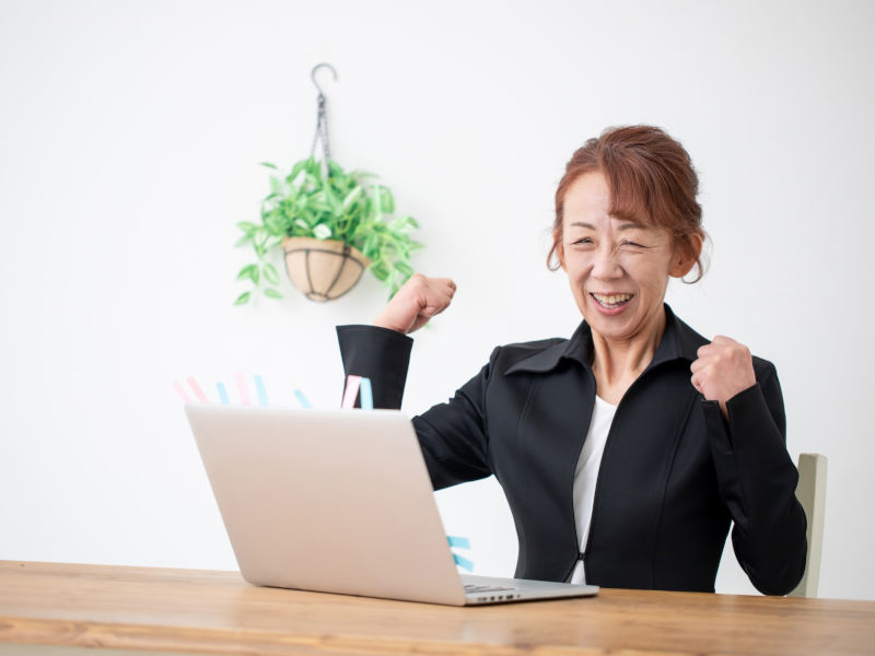 ご年配の女性がパソコンの前でガッツポーズしている写真